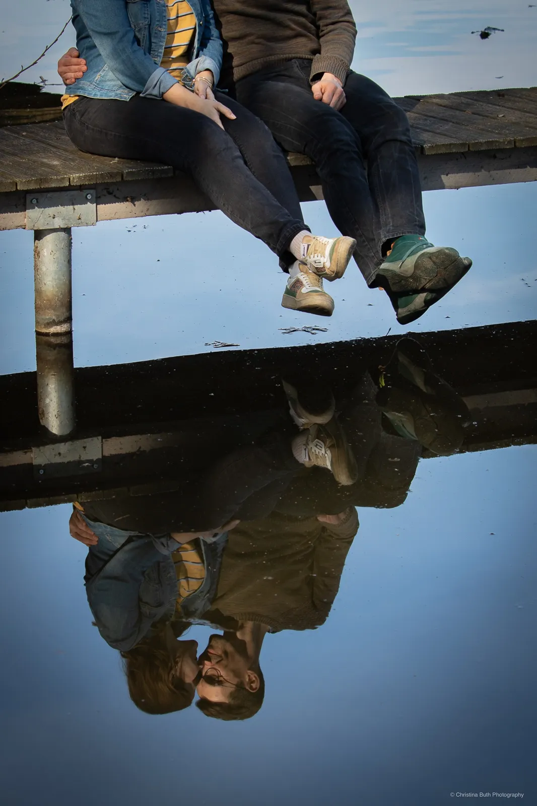 Paar sitzt auf einem Steg, Spiegelung im Wasser